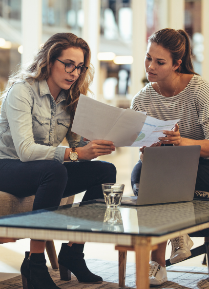 Two women discussing work infront of a laptop and sat on a sofa in the office