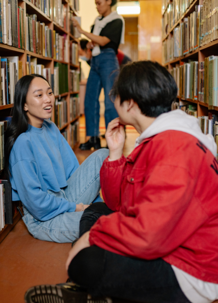 Two students sat in a library between the books and talking