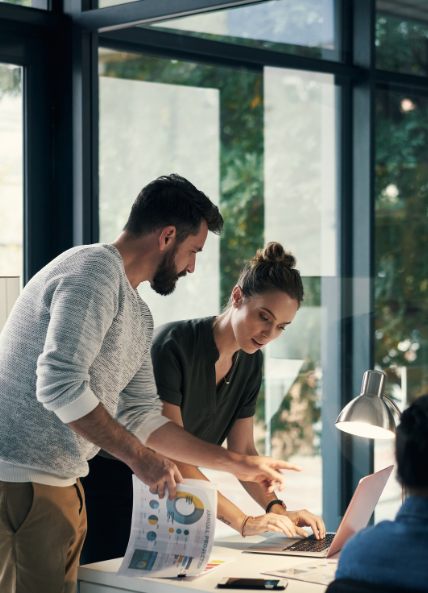 Two people chatting in an office with a laptop and strategy documents